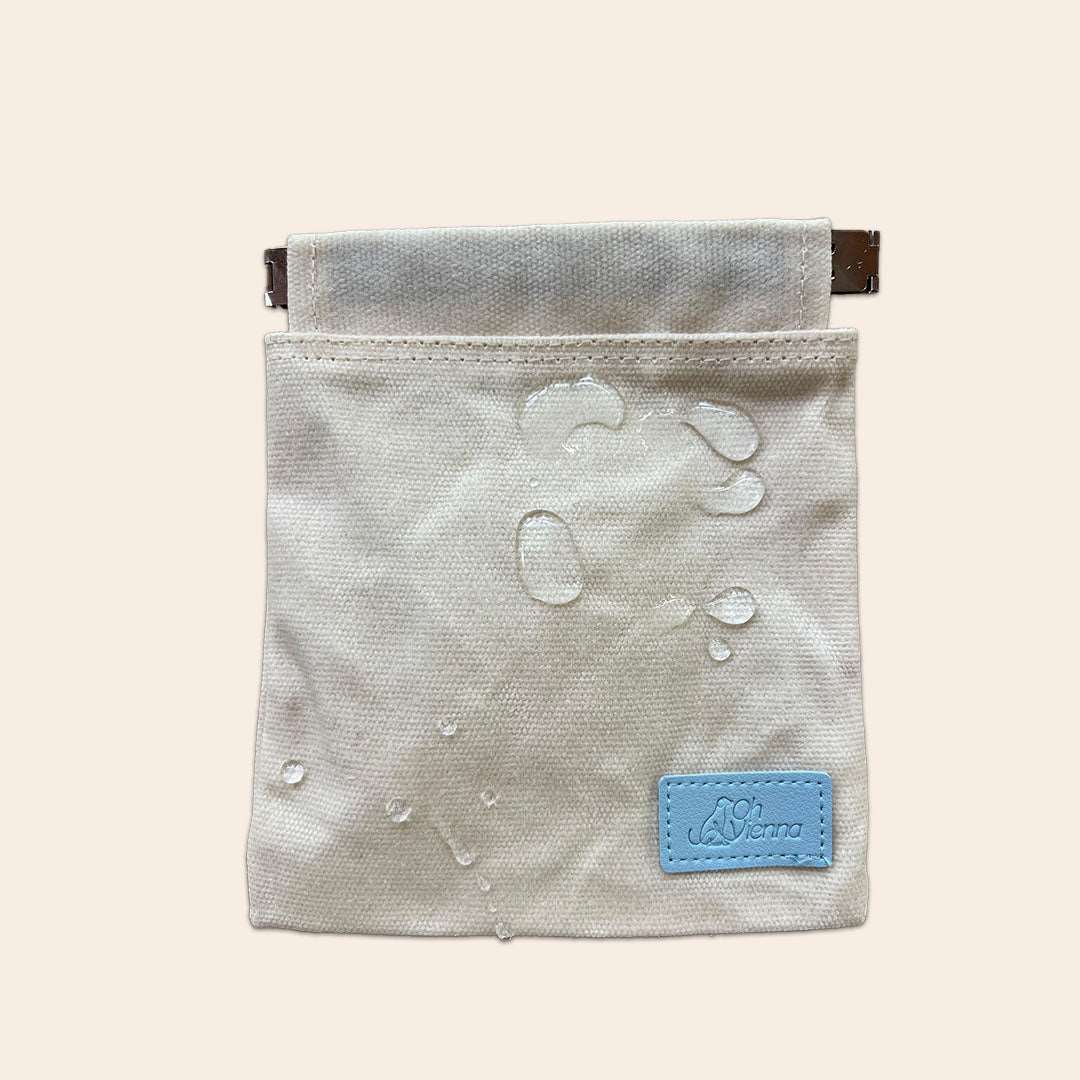 Beige canvas dog treat bag featuring a blue Oh Vienna logo and a convenient squeeze pouch closure with water droplets showing that it is waterproof