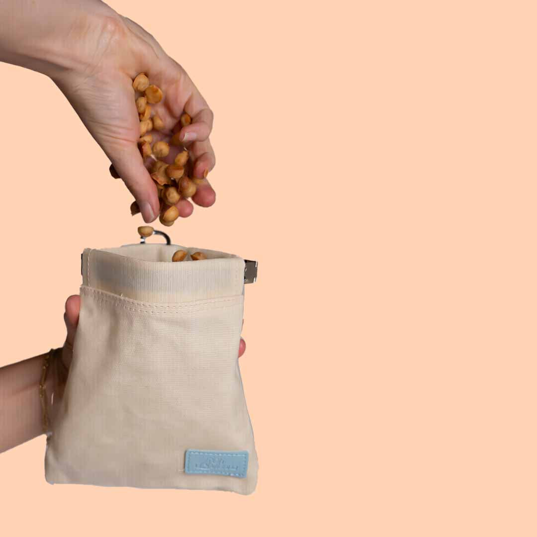 Beige canvas dog treat bag featuring a blue Oh Vienna logo and a convenient squeeze pouch closure. With  peach background