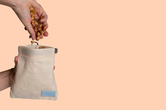 Hand pouring dog treats into a dog treat bag with a peach background